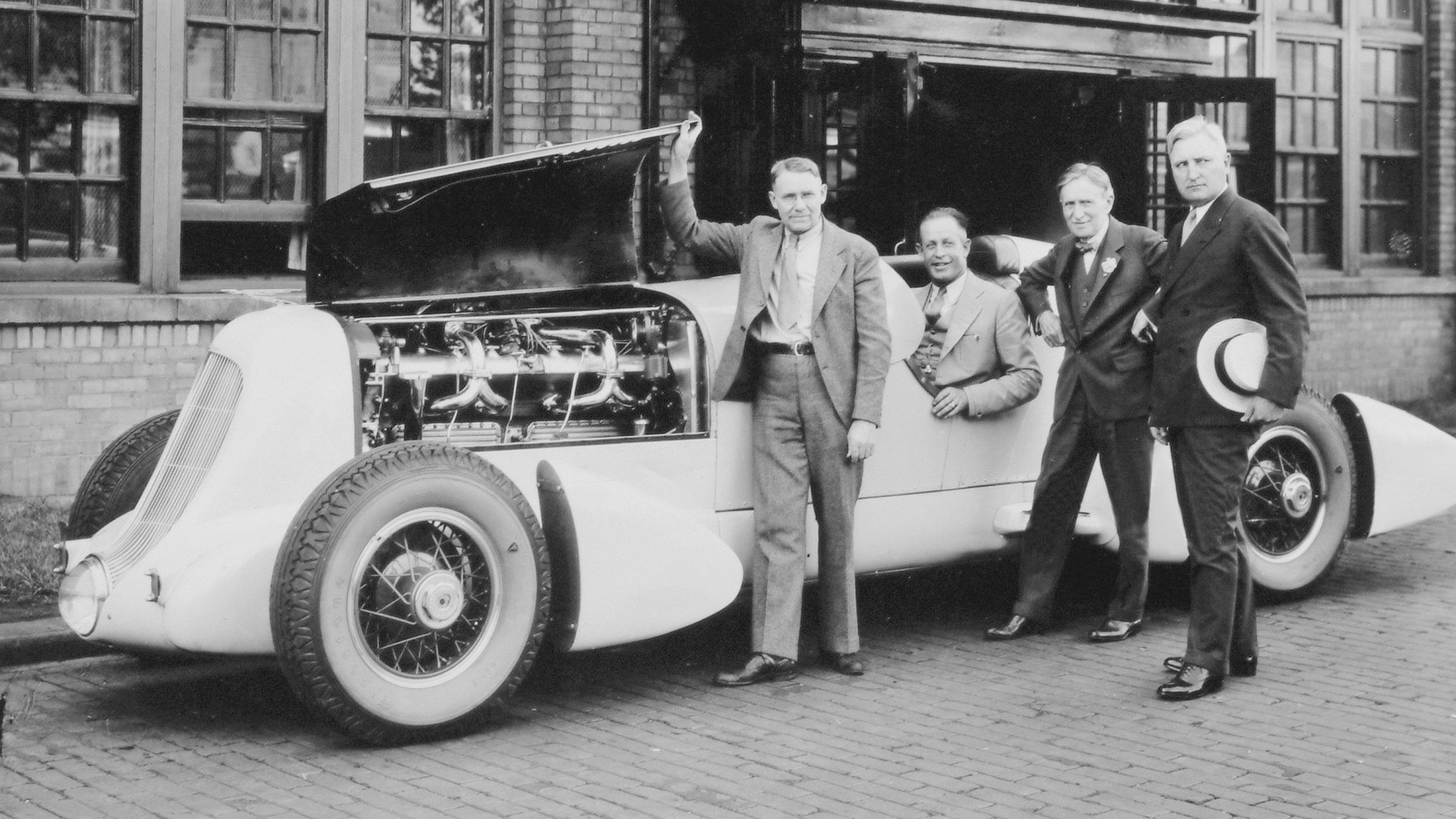 Duesenberg SJ Mormon Meteor Speedster frente al edificio de Firestone Tire & Rubber Co. De izquierda a derecha, Augie Duesenberg, Ab Jenkins, Harvey Firestone y un empresario desconocido. - Estados Unidos, 1935.